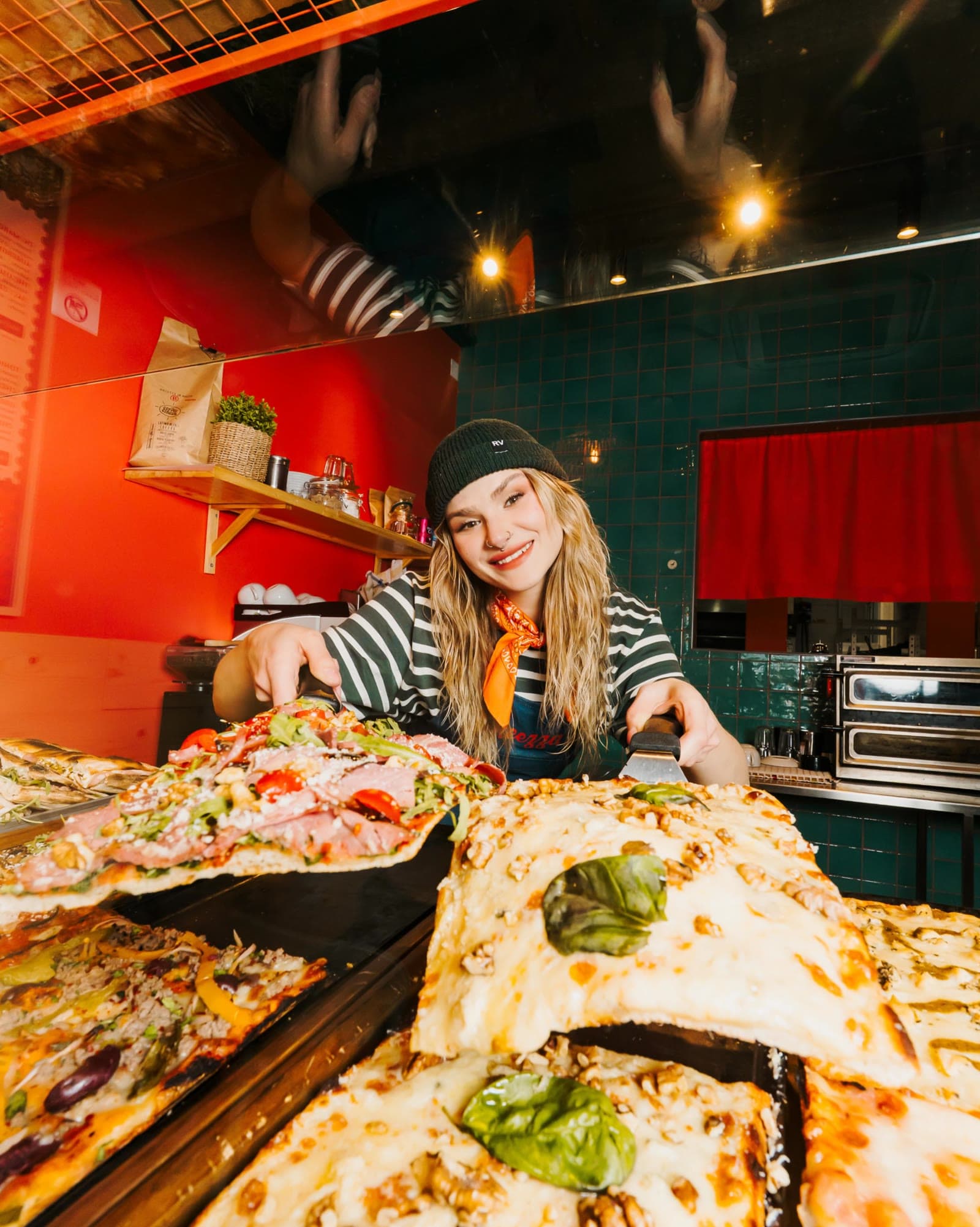 Steezza staff pulling a cheesy Roman-style slice from a fresh tray at the counter
