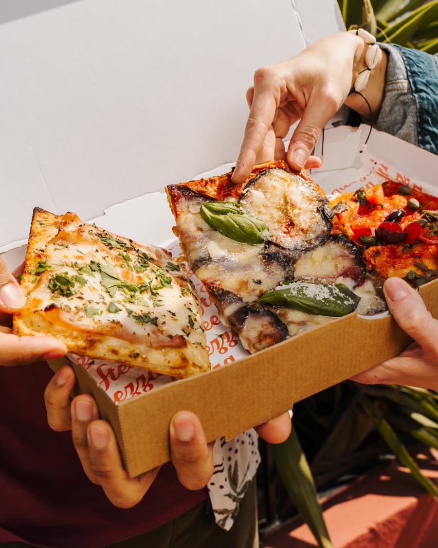 Hands sharing slices from a Steezza takeaway box